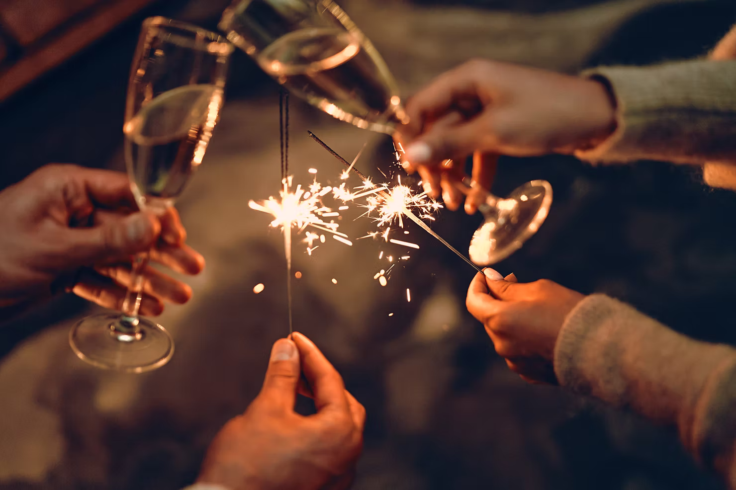 Hands holding sparklers and champagne glasses