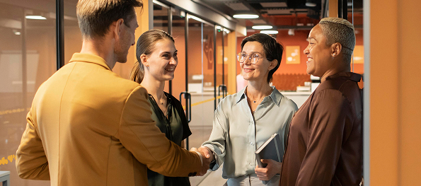Four people shaking hands and smiling in office hallway