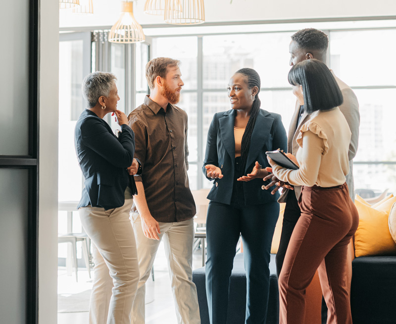 A group of five professionals standing and engaged in conversation in a modern, bright office.